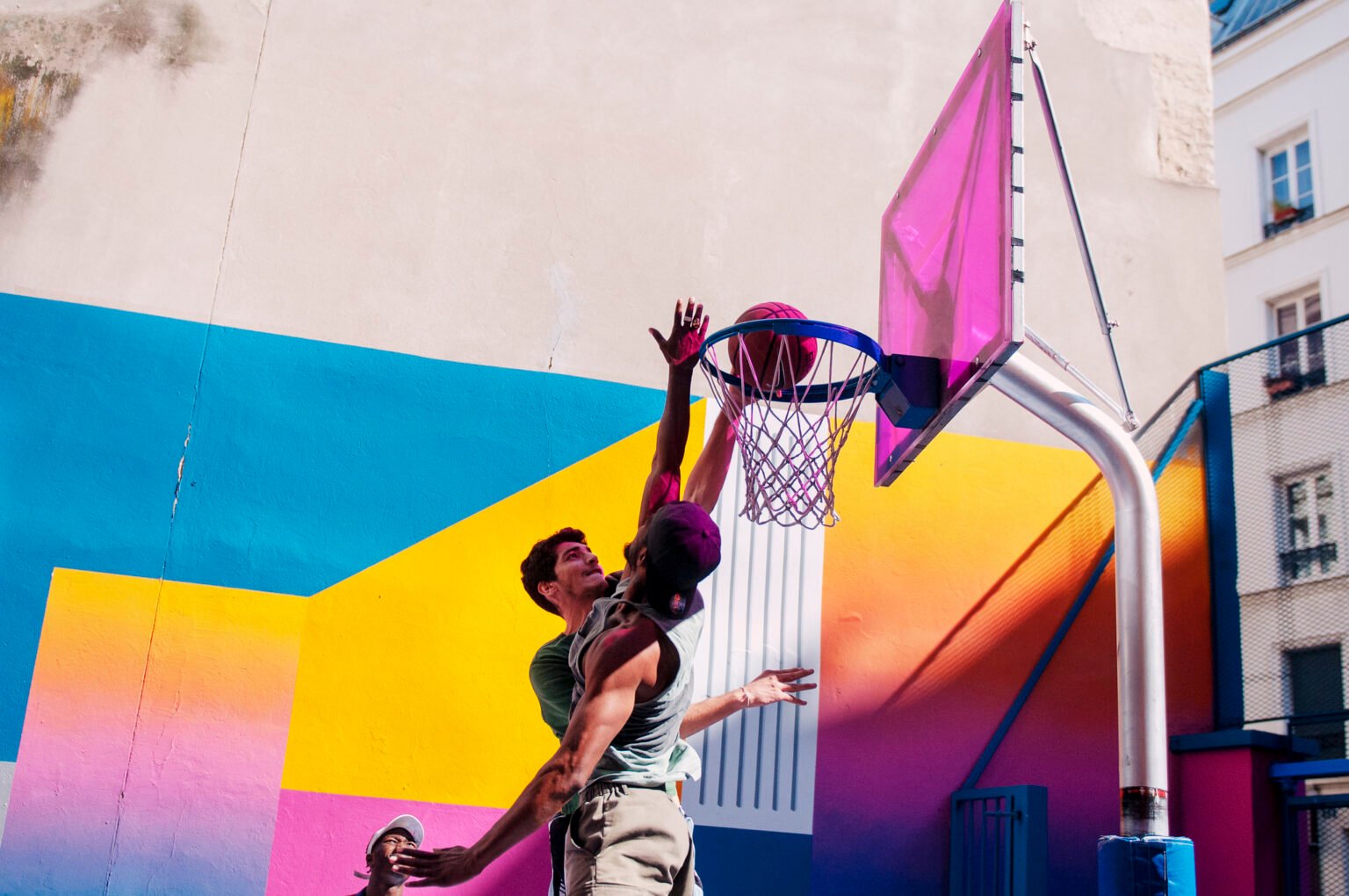 Dos jugadores saltando hacia la canasta en una pista de baloncesto con un mural de colores