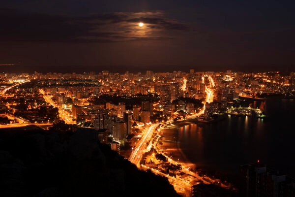 Vista elevada de Alicante iluminada de noche bajo la luna llena