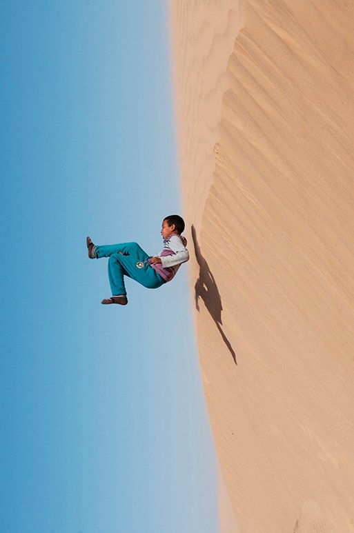 Niña saltando por la ladera de una duna de arena bajo un cielo azul